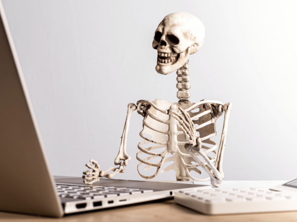 Skeleton seated at a desk with a laptop, depicting long website loading times