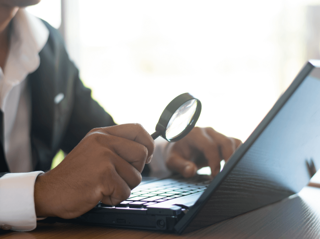 Person examining a laptop screen closely with a magnifying glass, searching for details